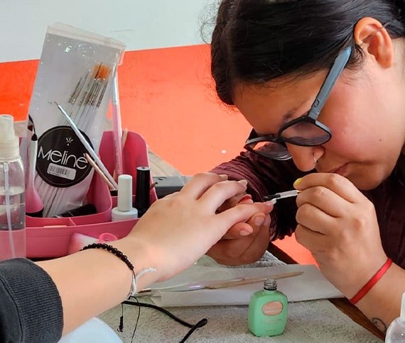 Una persona recibiendo una manicura; se aplica esmalte de uñas mientras herramientas y accesorios están organizados sobre la mesa.