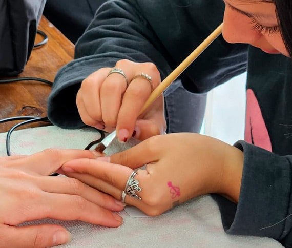 Primer plano de una manicura en proceso, con una persona aplicando esmalte en las uñas mientras utiliza un pincel fino. Las manos están sobre una toalla.